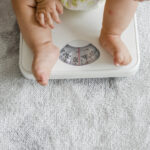 Obesidade infantil avança no país e exige atenção precoce, alerta especialista Closeup of a baby's legs on a weighing scale